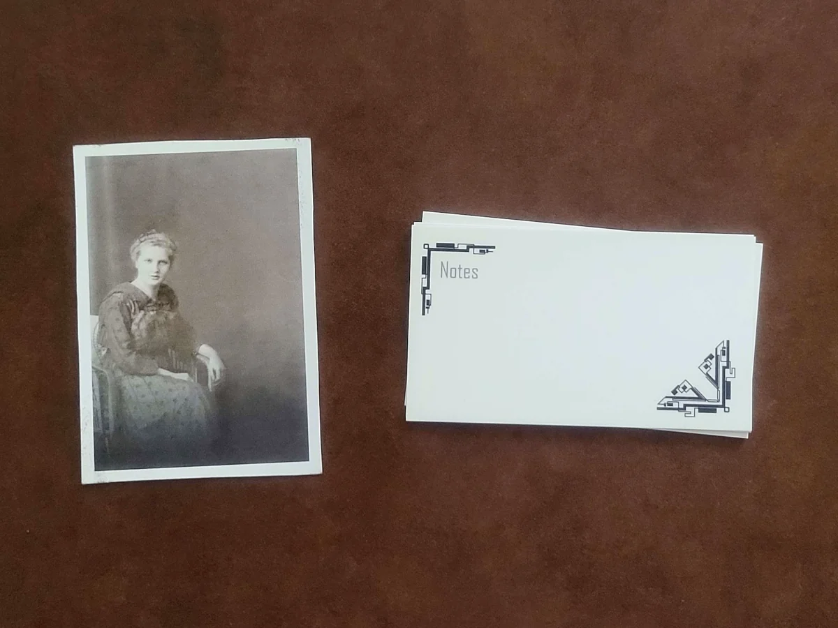 A printed old-fashioned photograph of a seated woman, next to a stack of business cards with an abstract black-and-white design in the corners.