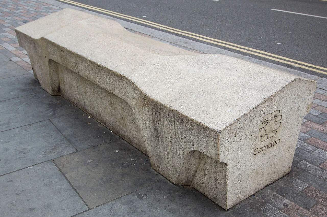 A grey concrete bench with a Camden logo on the side. The top has multiple sloping faces instead of a single flat surface.