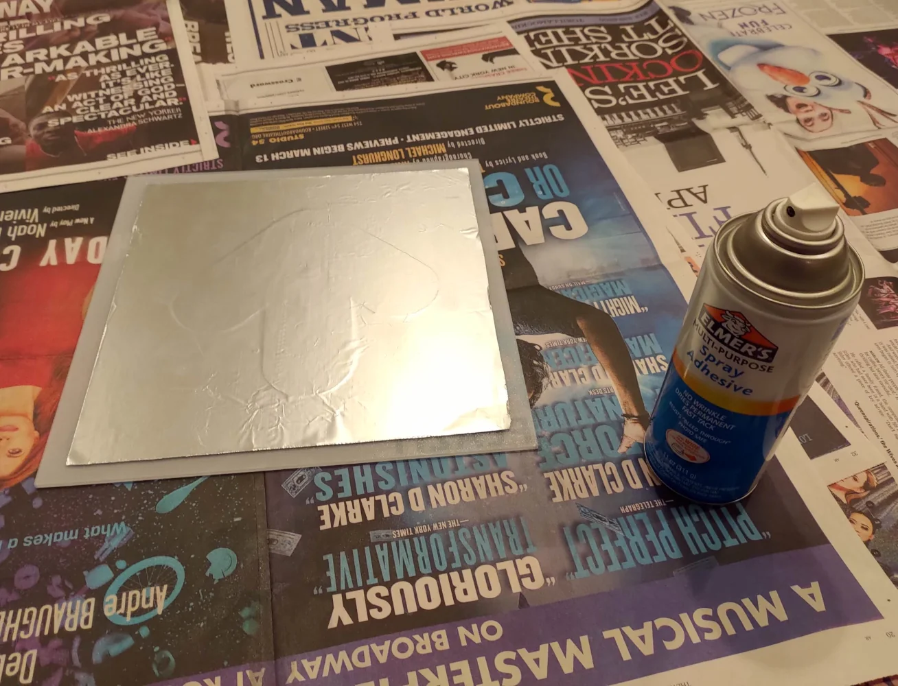A partially-complete pad panel next to a can of Elmer's brand spray glue. Both items are resting on a layer of newspaper.